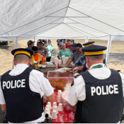 Des policiers servent de la nourriture et des boissons sous un auvent blanc à des personnes faisant la queue lors d'une activité en plein air.