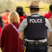 Un policier en uniforme vêtu d'un gilet portant l'inscription « POLICE » est à l'extérieur avec un groupe de personnes vêtues de chandails rouges.