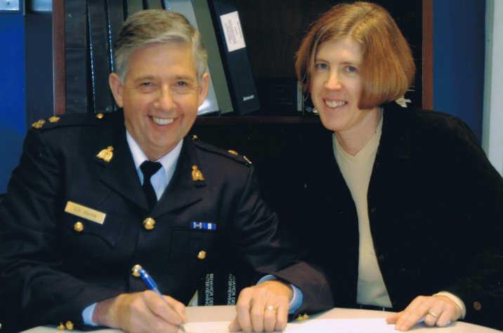 Une employée civile signe des documents à côté d’un policier de la GRC dans un bureau. 