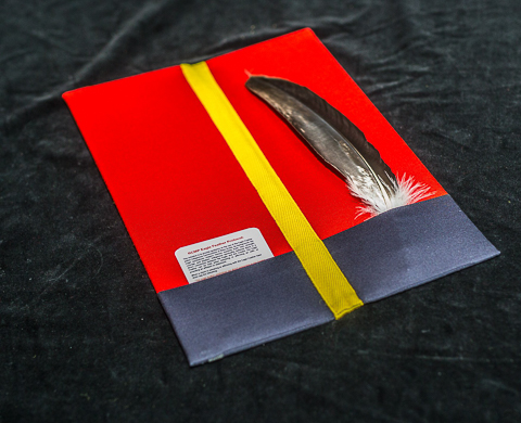 Une plume d’aigle repose dans une chemise rouge et bleue entourée d’un ruban jaune.