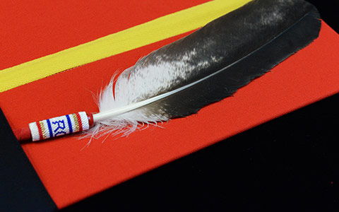 Une plume d'aigle est posée sur un dossier rouge entouré d'un ruban jaune.