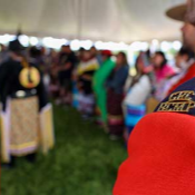 Le flash d'épaule d'un membre de la <abbr>GRC</abbr> en tunique rouge est montré en marge d'un arrière-plan flou d'une danseuse lors du Pow Wow des Premières Nations d'Abegweit.