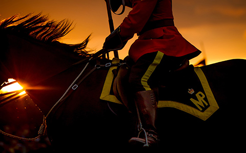 Un policier en tunique rouge monté sur un cheval noir alors que le soleil se couche derrière eux