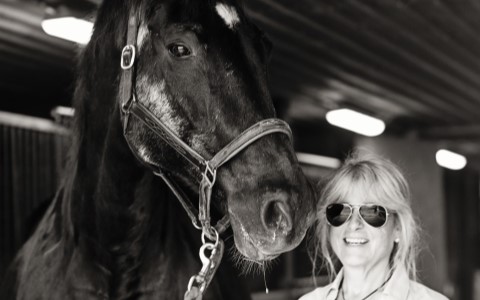 Un jeune cavalier en selle serre le cou d'un cheval noir âgé.