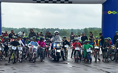 Un agent de la GRC à moto au milieu des cyclistes sur la ligne de départ d’une course.