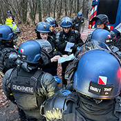 Des policiers en uniforme à côté d'un véhicule discutent de stratégies en consultant des plans sur papier.