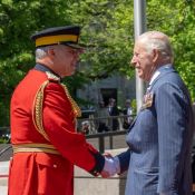 Un officier haut gradé en tunique rouge serre la main du roi Charles III.
