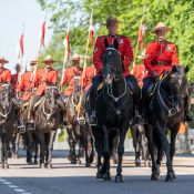 Deux membres de la police montée mènent une escorte de cavaliers portant des drapeaux.