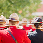 Des cadets en tunique rouge coiffés de chapeaux Stetson. Il y a aussi une cadette d'un autre service de police en uniforme noir.