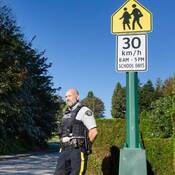 Un agent de la GRC fait respecter la limite de vitesse dans une zone scolaire, un panneau dans le coin supérieur droit indiquant que cette limite est de 30 km/h.