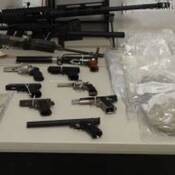 Photo d’une table sur laquelle se trouvent les armes à feu, l’argent en espèces et les drogues illicites saisis lors de perquisitions dans des propriétés de Surrey et de Richmond.