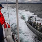Un membre en uniforme de la Garde côtière canadienne à bord d’un navire observe un zodiac gris de la GRC, avec à son bord quatre membres du Groupe tactique d’intervention.