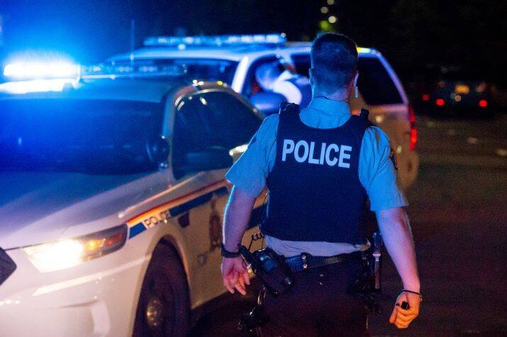 A male RCMP officer approaching a police car at night.