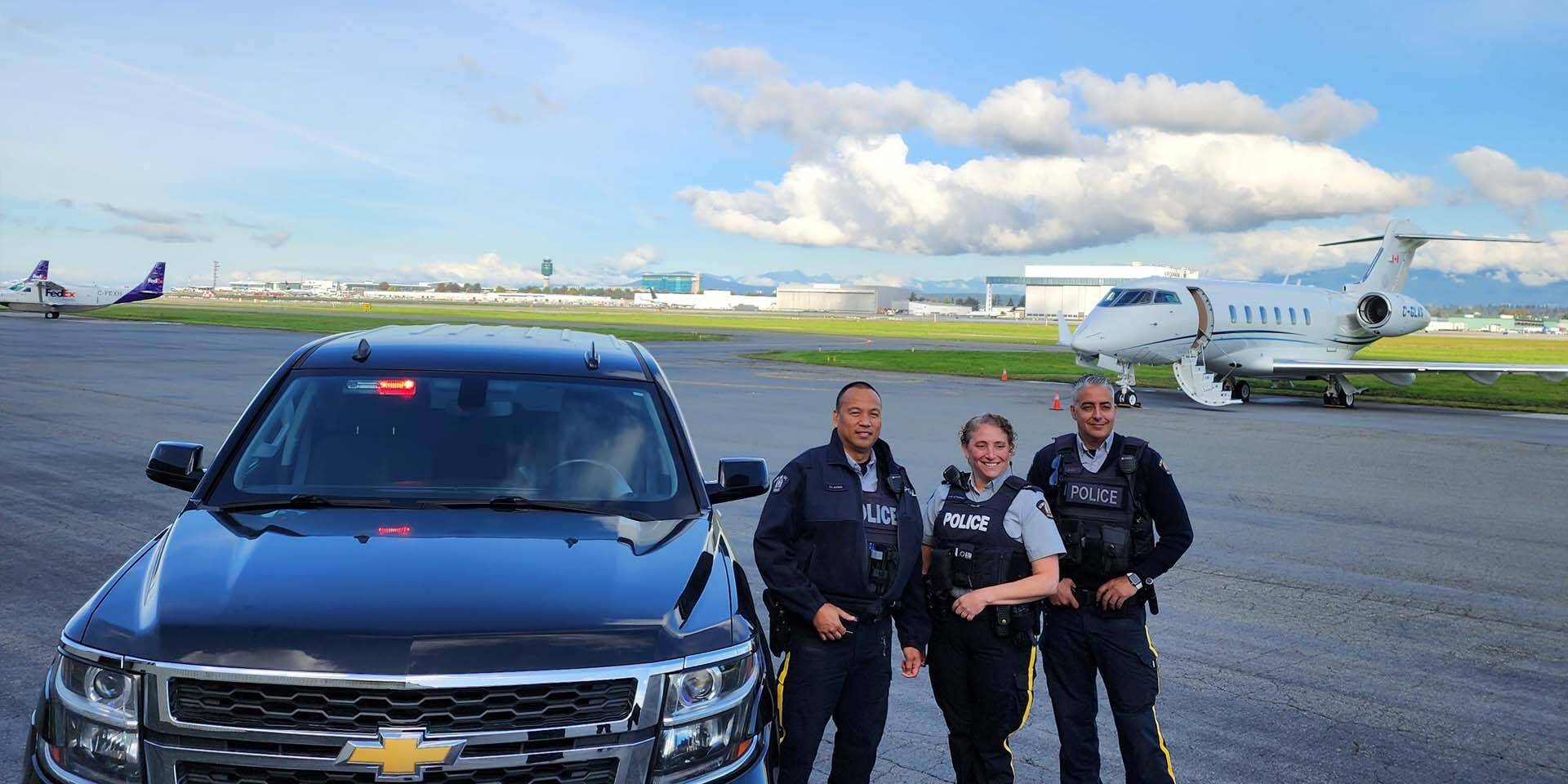 Des agents de la GRC de Richmond se tiennent debout à côté d’une camionnette et des avions sont en arrière-plan.