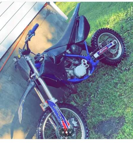 A blue and black dirt bike leaning against the foundation of a structure.